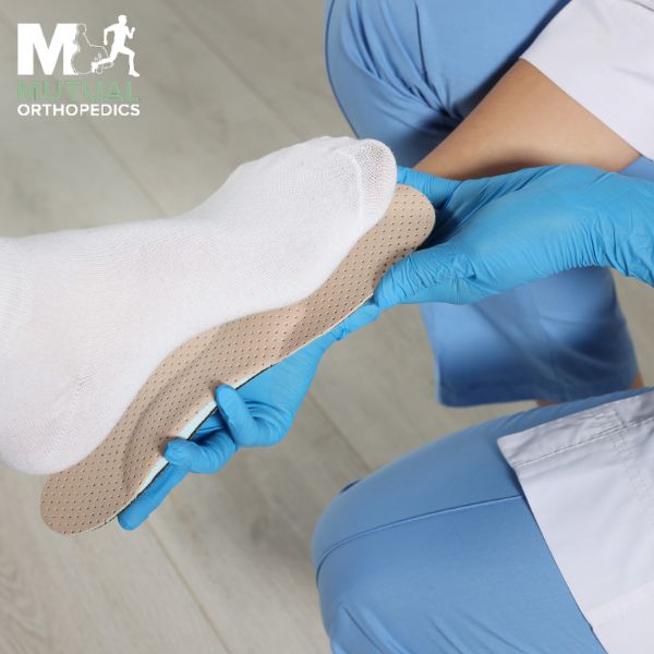 A medical professional in blue gloves fits a custom insole under a patient's sock covered foot
