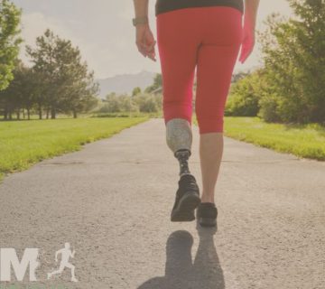 A person with a prosthetic leg walks on a paved path in a park, wearing red leggings and black shoes The scene is sunny with greenery on both sides