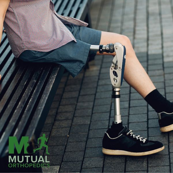 Person with a prosthetic leg sits on a bench outdoors The logo for Mutual Orthopedics is displayed in the bottom left corner